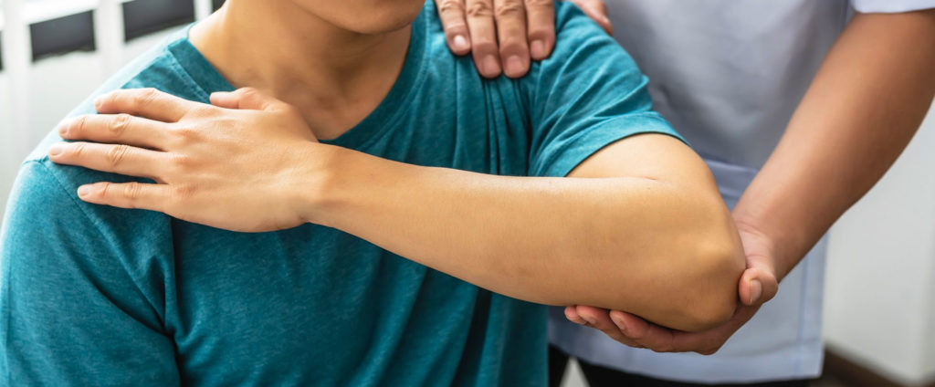 chiropractor moving the shoulder of young man in turquoise tshirt